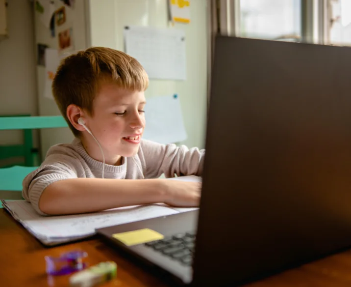 A primary school student smiling during an online lesson on a laptop
